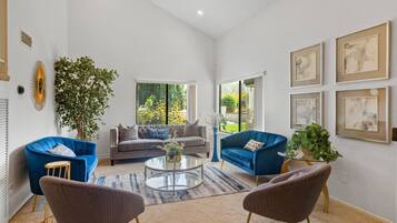 A spacious living room with a large window, a blue sofa, a grey sofa, a coffee table, and a potted plant.