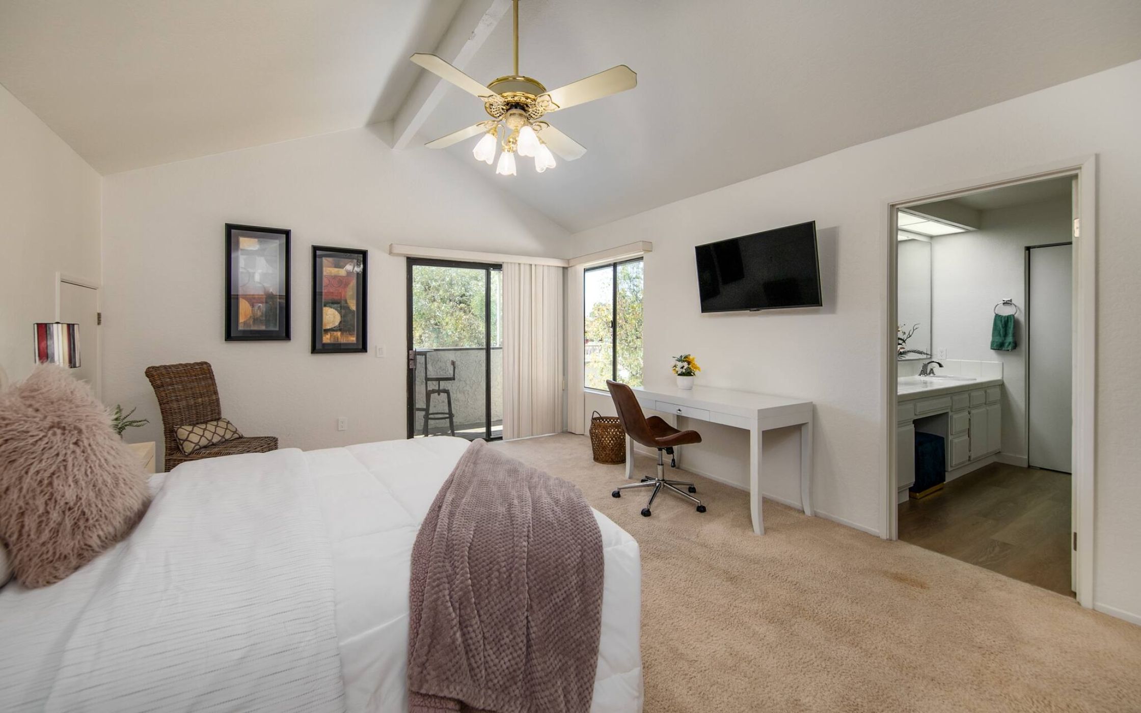 A hotel room with a bed, a desk, a chair, a TV, and a bathroom.