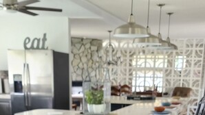 A modern kitchen with a central island, stainless steel appliances, pendant lighting, and a decorative wall. - Mid-Century Family Home - Corporate Relocatio  Rental (Charlotte)