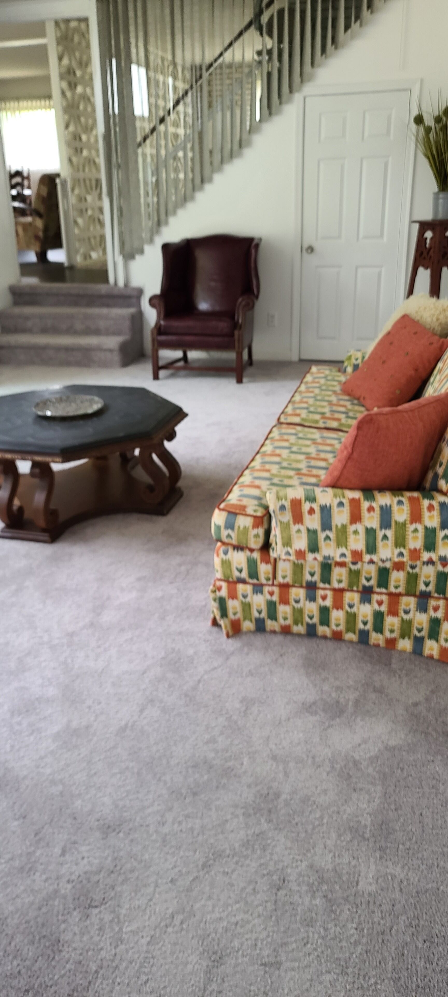 Una sala de estar con un sofá estampado, una mesa de centro de madera y una escalera al fondo.