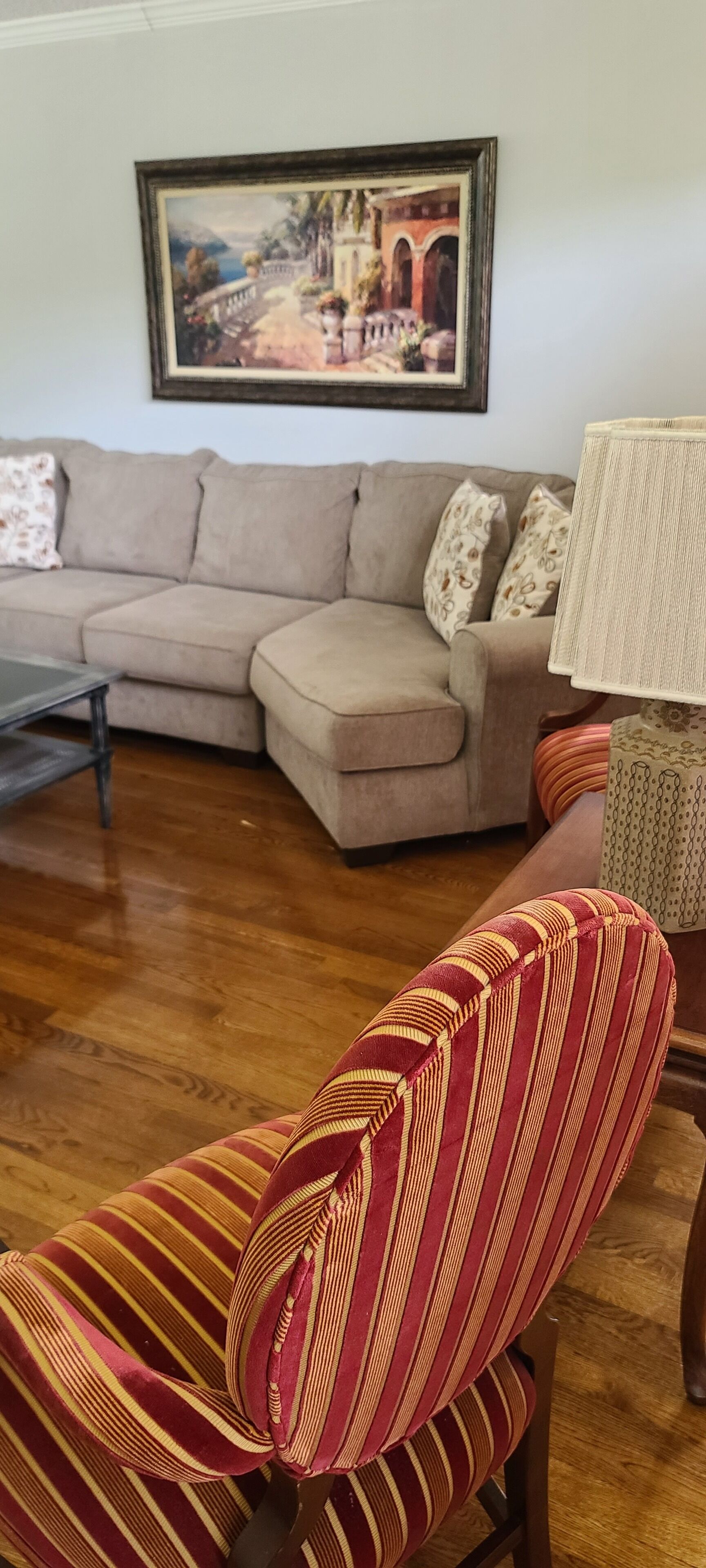 Una sala de estar con un sofá seccional color beige, un sillón a rayas, una mesa de centro de madera y un cuadro enmarcado en la pared.