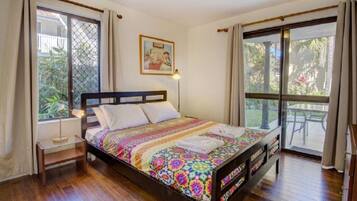 A bedroom with a wooden bed, a bedside table, a lamp, and a large window with curtains.