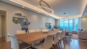 A modern dining area with a wooden table and white chairs, a large mirror, and a view of the sea through large windows. - The Stylish Apt. of Madeira Palace CC (Funchal)