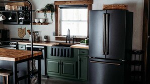 A kitchen with a black refrigerator, wooden cabinets, a sink, and a window.