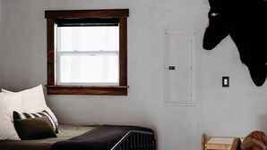 A bedroom with a sloped ceiling, a bed with a black headboard, a window, a mounted animal hide, a small table, and a leather chair.