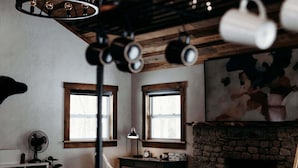 A rustic room with a fireplace, two windows, a sofa, and a table with a lamp.