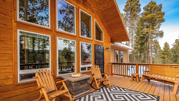 Une terrasse en bois avec deux fauteuils à bascule, un foyer et un tapis à motifs.