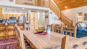 A spacious kitchen with wooden cabinets, a dining area with a large table, and a staircase leading to an upper level. - Dog Friendly w/Guesthouse, Deck w/Grill, Foosball, Trail Access, Kid's Playhouse (Angel Fire)