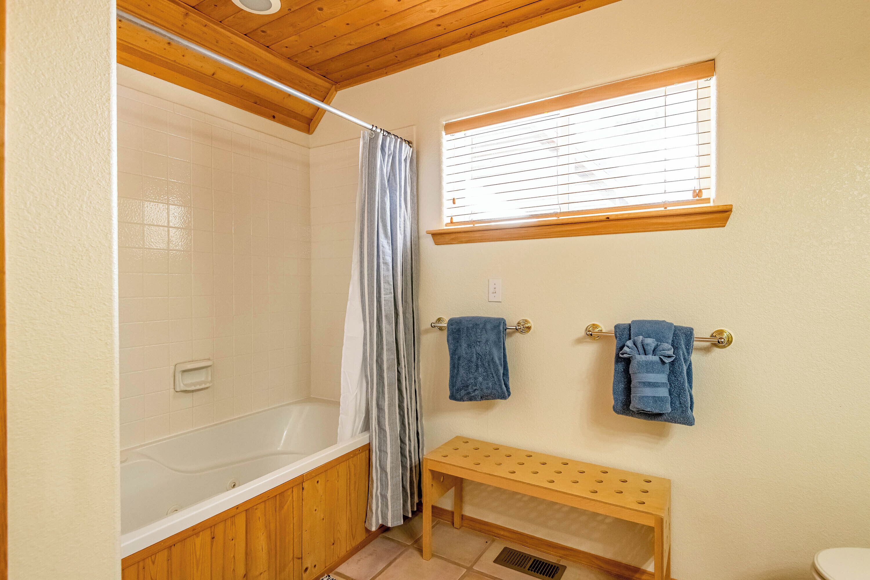 Een badkamer met een bad, een douchegordijn, een raam en een houten bankje.
