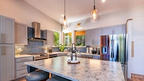 Una cocina moderna con una isla grande, electrodomésticos de acero inoxidable e iluminación colgante.
