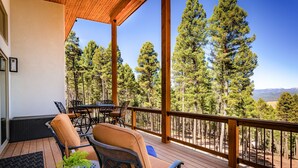 Una terraza de madera con mobiliario exterior, vistas a altos pinos y un cielo despejado.