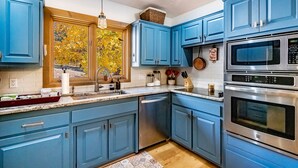 A kitchen with blue cabinets, stainless steel appliances, and a window with autumn leaves. - Spacious Townhouse, Firepit, Walkable to Park/Golf/Tennis, Foosball, Two Decks (Angel Fire)
