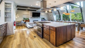 A modern kitchen with a large island, wooden cabinetry, and a dining area with a view. - Modern Lodge w/Hot Tub, Beautiful View, Foosball, 2 Car Garage, Gourmet Kitchen (Angel Fire)