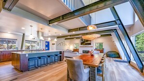 A modern kitchen with a central island, bar seating, and a dining area with a large wooden table. - Modern Lodge w/Hot Tub, Beautiful View, Foosball, 2 Car Garage, Gourmet Kitchen (Angel Fire)