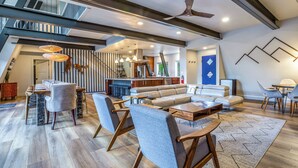 A spacious living area with a dining table, sofas, and a staircase leading to an upper level. - Modern Lodge w/Hot Tub, Beautiful View, Foosball, 2 Car Garage, Gourmet Kitchen (Angel Fire)