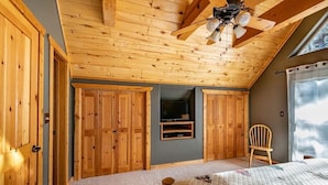 Quarto com vigas de madeira no teto, uma cama, uma televisão e uma cadeira.