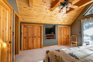 A bedroom with wooden ceiling beams, a bed, a TV, and a chair.