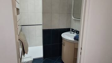 A small bathroom with a white sink, a mirror, and a shower area.