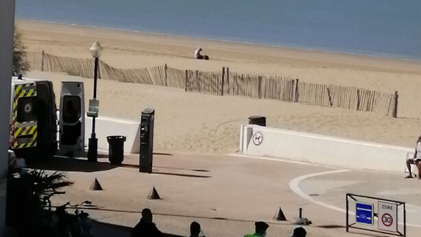 Une vue sur la plage, avec un rivage sablonneux, une clôture en bois et quelques personnes.
