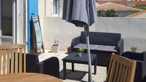 Un espace extérieur aménagé avec des meubles en osier, une table et un parasol bleu.