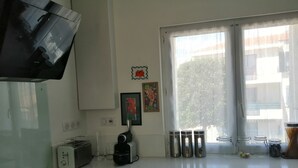 Une cuisine moderne équipée d’une cuisinière intégrée, d’un grille-pain et d’une machine à café. On y trouve trois récipients en acier inoxydable sur le plan de travail, ainsi qu’une fenêtre ornée de rideaux légers.