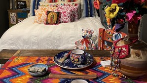 A cozy bedroom with a bed, colorful pillows, a decorative vase, and a tray with a cup and saucer.