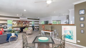 Una sala de estar moderna con una mesa de comedor de vidrio, un sofá y una zona de cocina con ventanal.