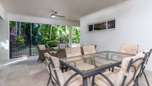 Un patio espacioso con una mesa de vidrio y seis sillas, rodeado por un muro blanco y vistas a abundante follaje.