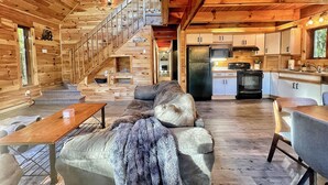 A cabin interior with a wooden staircase, a sofa, a dining table, and a kitchen area. - The Challenge House-mega games-hottub-beach-lake-The ultimate Poconos game house (Blakeslee)
