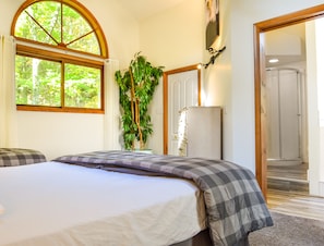 A bedroom with a bed, a large window, a plant, and a door leading to a bathroom.