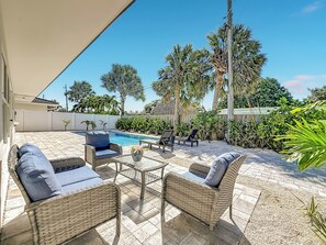 A patio area with a swimming pool, wicker furniture, and palm trees.