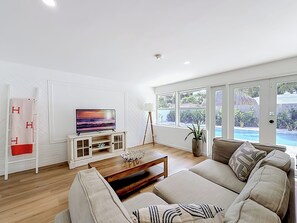 Een moderne woonkamer met een flatscreen televisie, een bank, een salontafel en uitzicht op een zwembad.