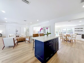 A spacious living area with a central island, a dining area with a view, and a kitchen with modern appliances.