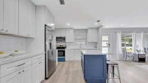 Una cocina moderna con armarios blancos, una isla central y un comedor con sillas.