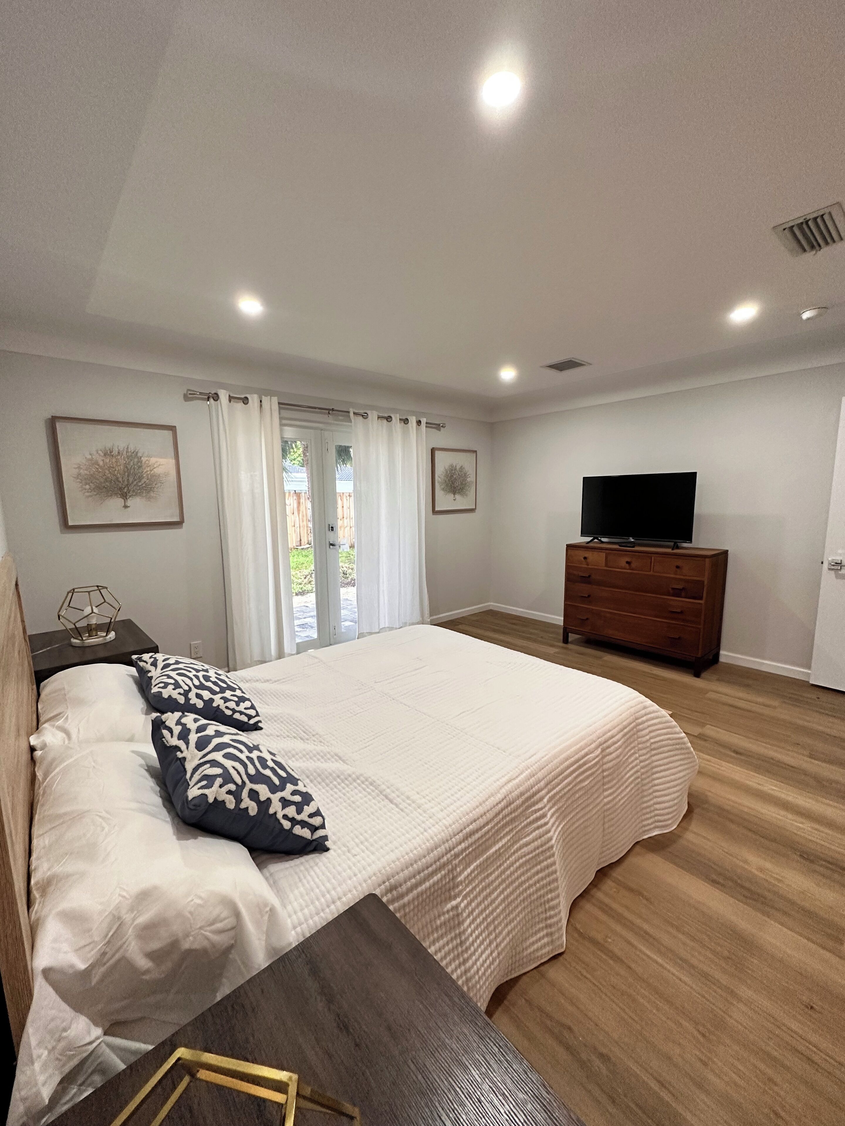 A bedroom with a bed, a dresser, a TV, and a window with curtains.