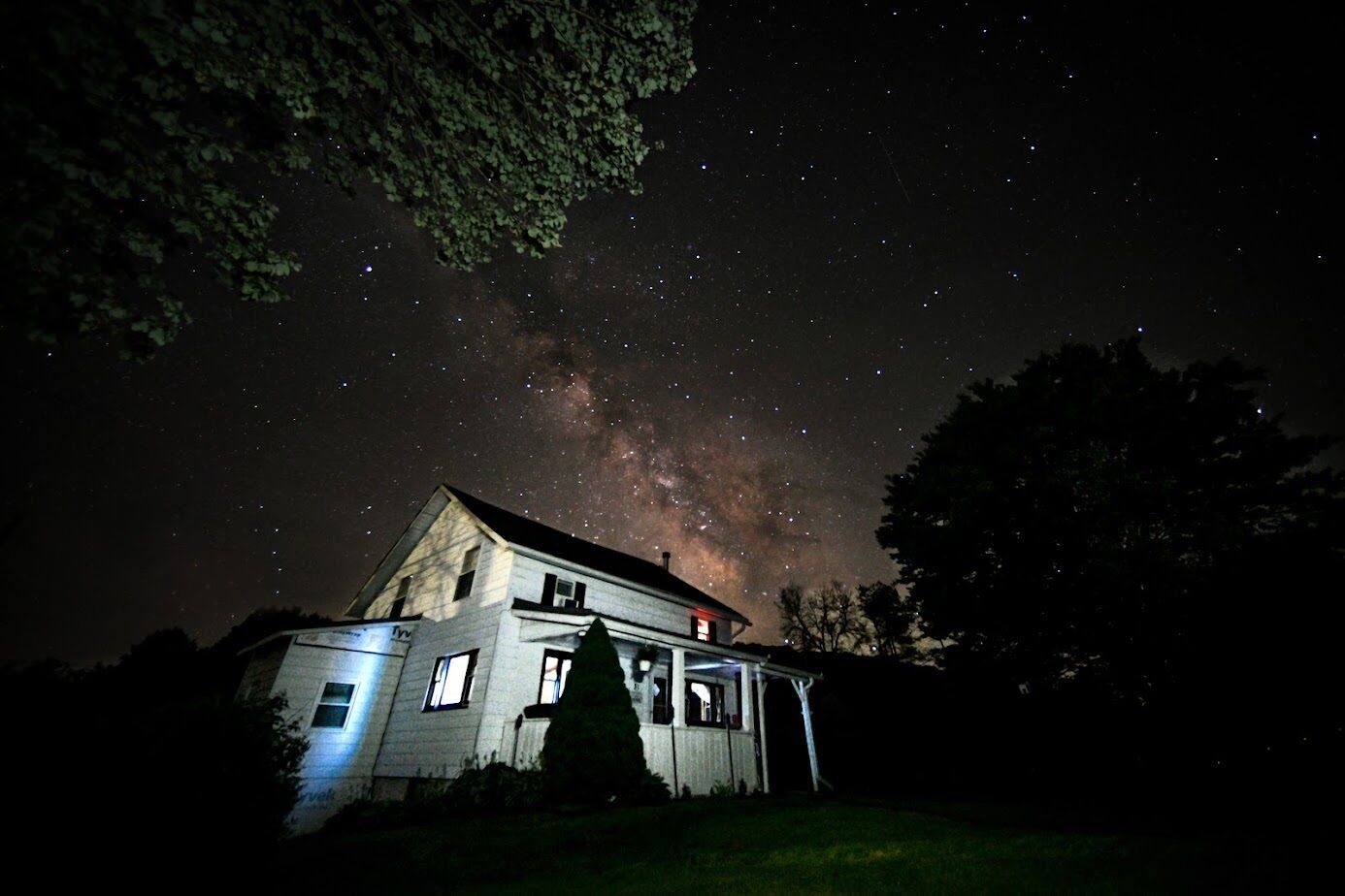 Una casa con porta e finestre ben visibili, circondata da alberi, sotto un cielo stellato.