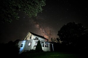 Una casa con porta e finestre ben visibili, circondata da alberi, sotto un cielo stellato.