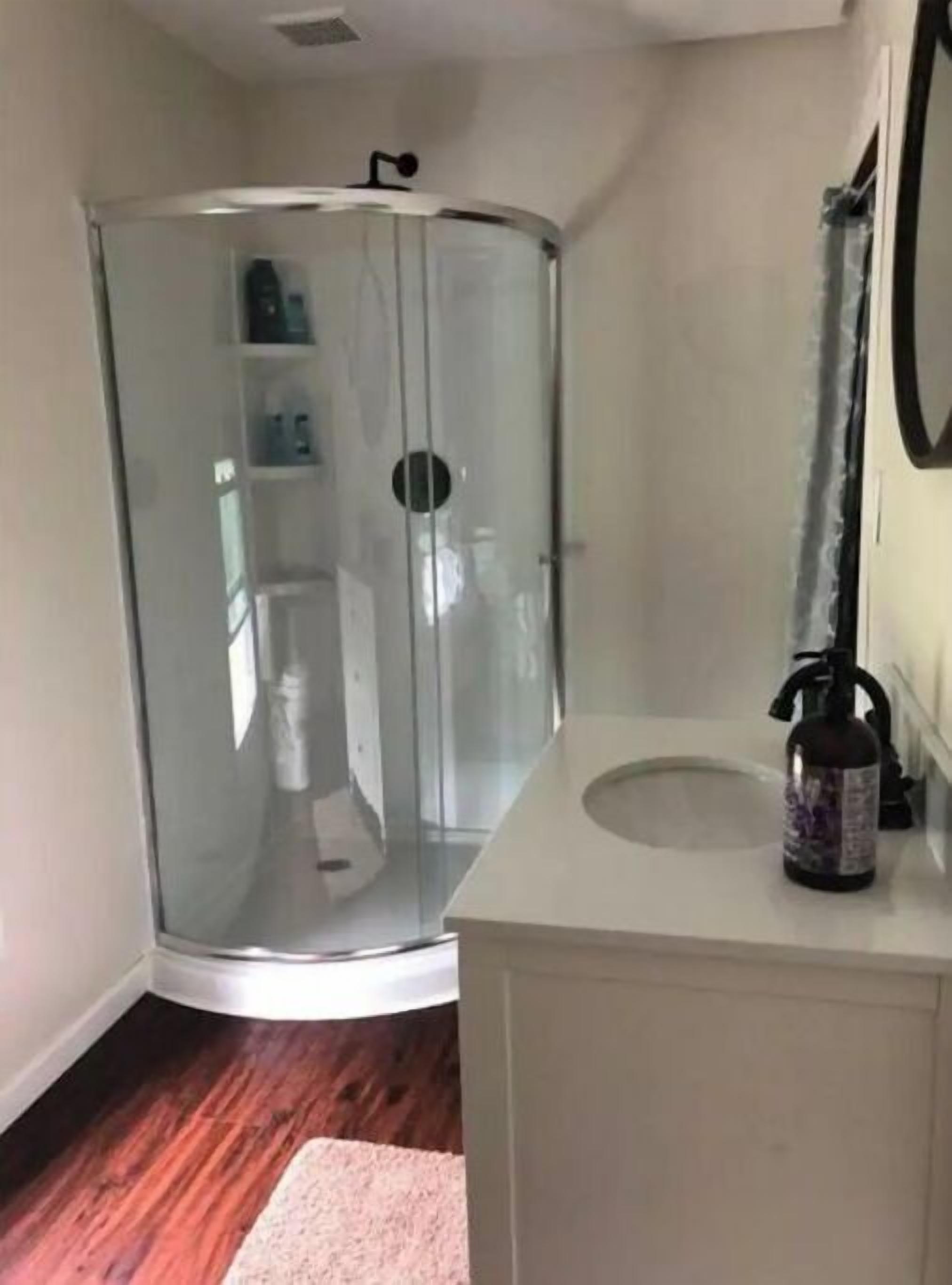 A bathroom with a glass shower enclosure, a white sink with a faucet, and a wooden floor.