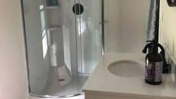 A bathroom with a glass shower enclosure, a white sink with a faucet, and a wooden floor.