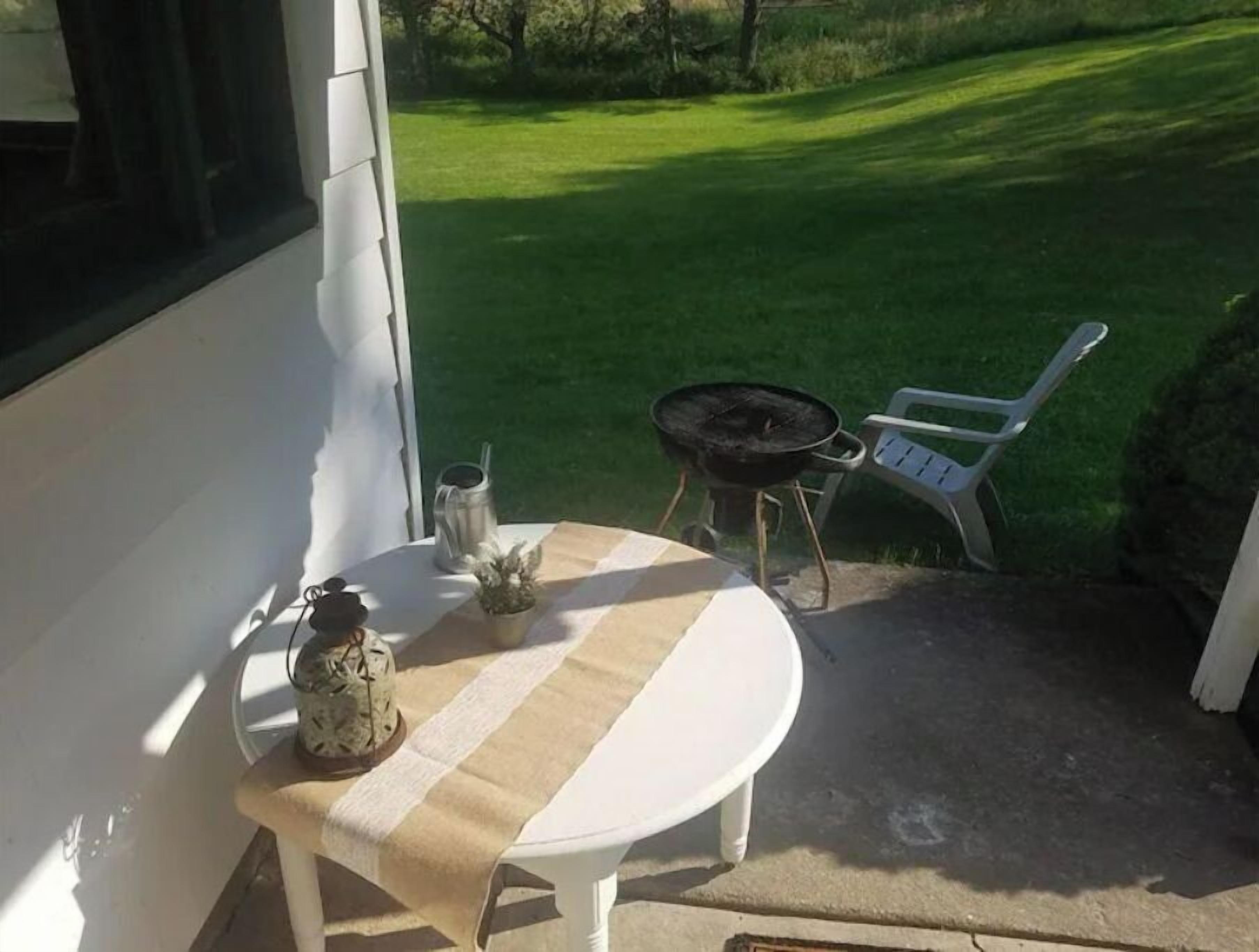 A patio with a table, a chair, a grill, and a decorative item.