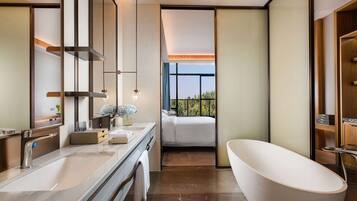 A modern bathroom with a large bathtub, a double sink, and a large mirror. There is a window providing a view of the outdoors.