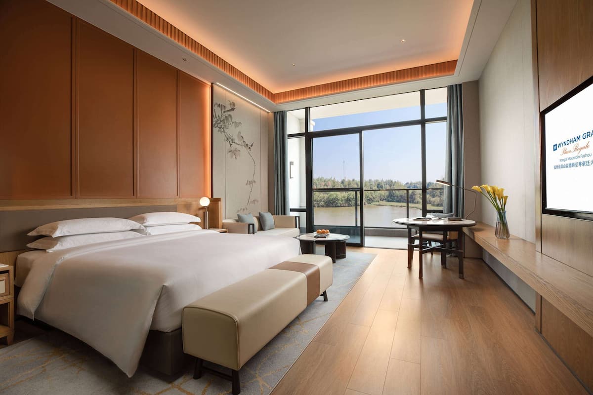 Ein modernes Hotelzimmer mit einem großen Bett, einer Sitzecke, einem Esstisch und Blick ins Freie.