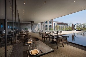 An outdoor dining area with tables and chairs, a pool, and a view of a building in the background. - Wyndham Grand Plaza Royale Xiangai Mountain Fuzhou (Fuzhou)