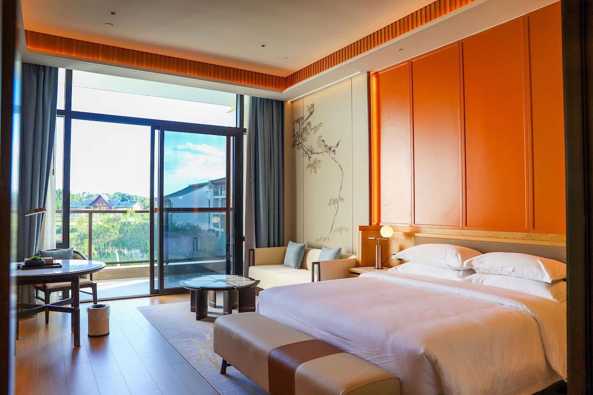 Ein Hotelzimmer mit einem großen Bett, einer Couch, einem kleinen Tisch und Blick ins Freie.