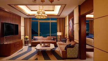 A spacious living room with a large flat-screen TV, a sofa set, a coffee table, and a view of the ocean.