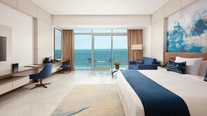 A hotel room with a large bed, a desk, a chair, a TV, and a view of the ocean. - Royal M Al Aqah Beach Hotel And Resort by Gewan (Al Aqah)