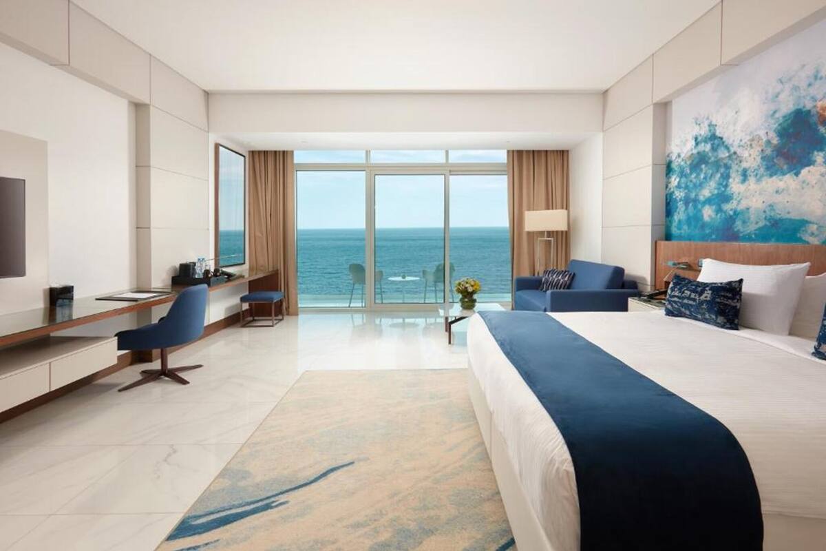 Quarto de hotel com uma cama grande, uma escrivaninha, uma cadeira, uma televisão e vista para o oceano.