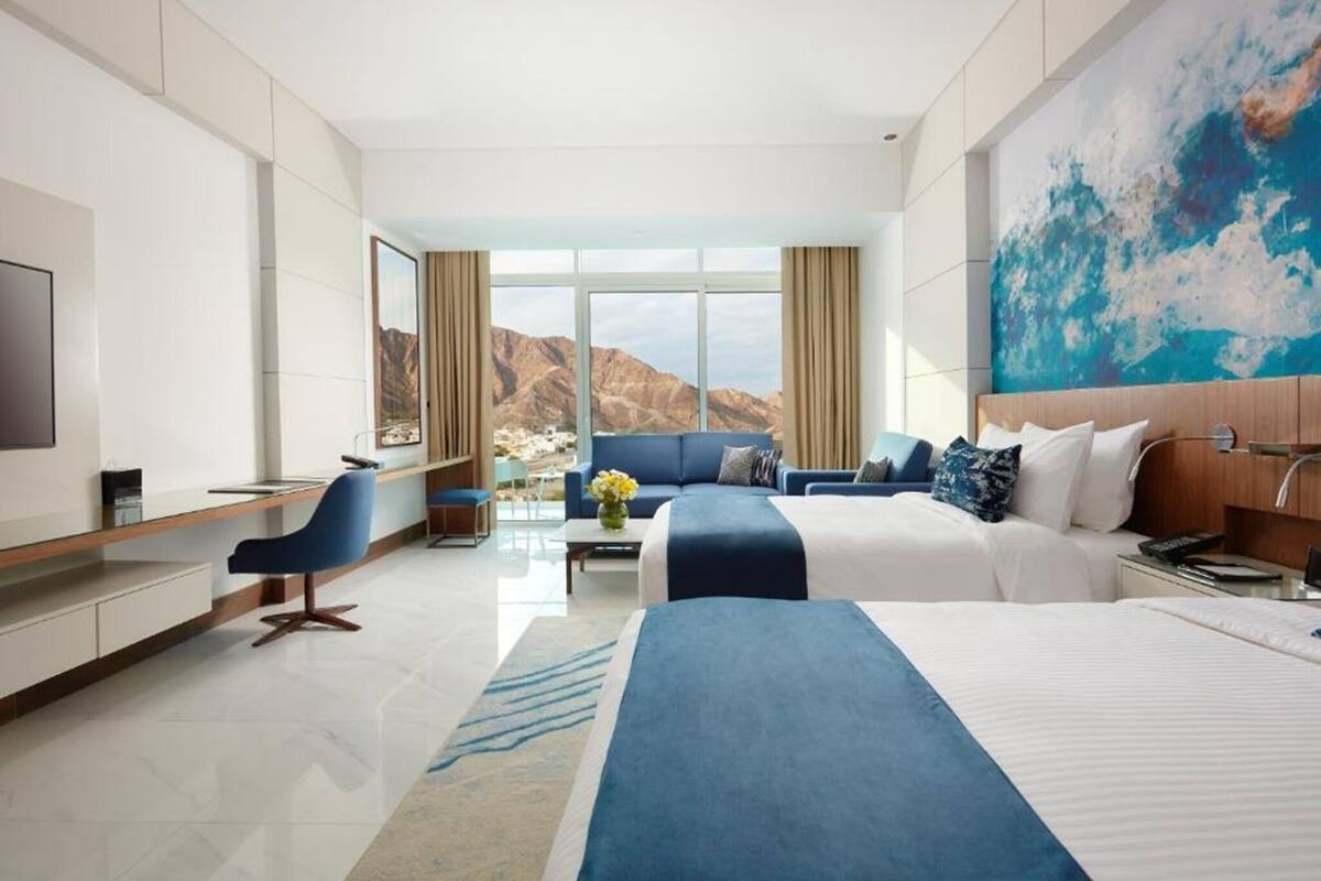 Quarto de hotel moderno com uma cama grande, um sofá, uma escrivaninha e uma televisão.