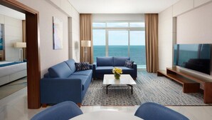 A modern hotel room with a large window offering a sea view, a sofa set, a flat-screen TV, and a coffee table. - Royal M Al Aqah Beach Hotel And Resort by Gewan (Al Aqah)