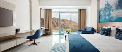 Una habitación de hotel moderna con una cama grande, un escritorio, una silla, un televisor y vistas a montañas.
